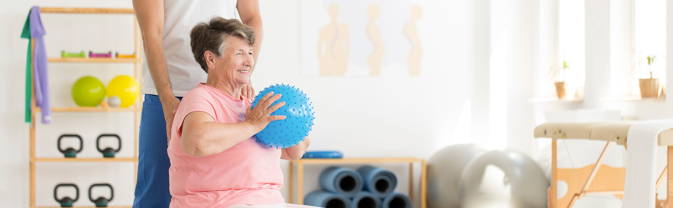 elderly lady holding a ball exercising with pink top on in a home gym