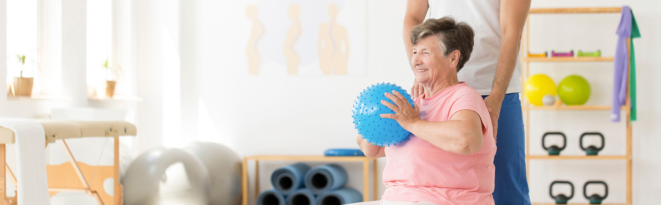 elderly lady holding a ball exercising with pink top on in a home gym